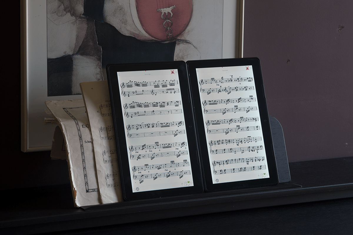 Scora Doble Tabletten auf Klavier mit Papierbüchern dahinter
